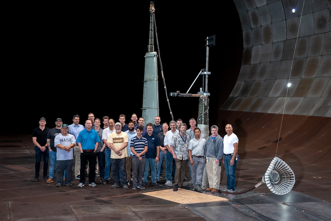 The team responsible for the testing of the integrated Actively Stabilized Refueling Drogue System and Optical Reference System stands with the tested hose and drogue system in the 40- by 80-foot wind tunnel at the Arnold Engineering Development Complex National Full-Scale Aerodynamics Complex, located in the NASA Ames Research Center at Moffett Field in Mountain View, California. The NFAC test team consisted of both Department of Defense and Test Operations and Sustainment contract employees from National Aerospace Solutions. The team included researchers, engineers, technicians and mechanics. (Courtesy photo)