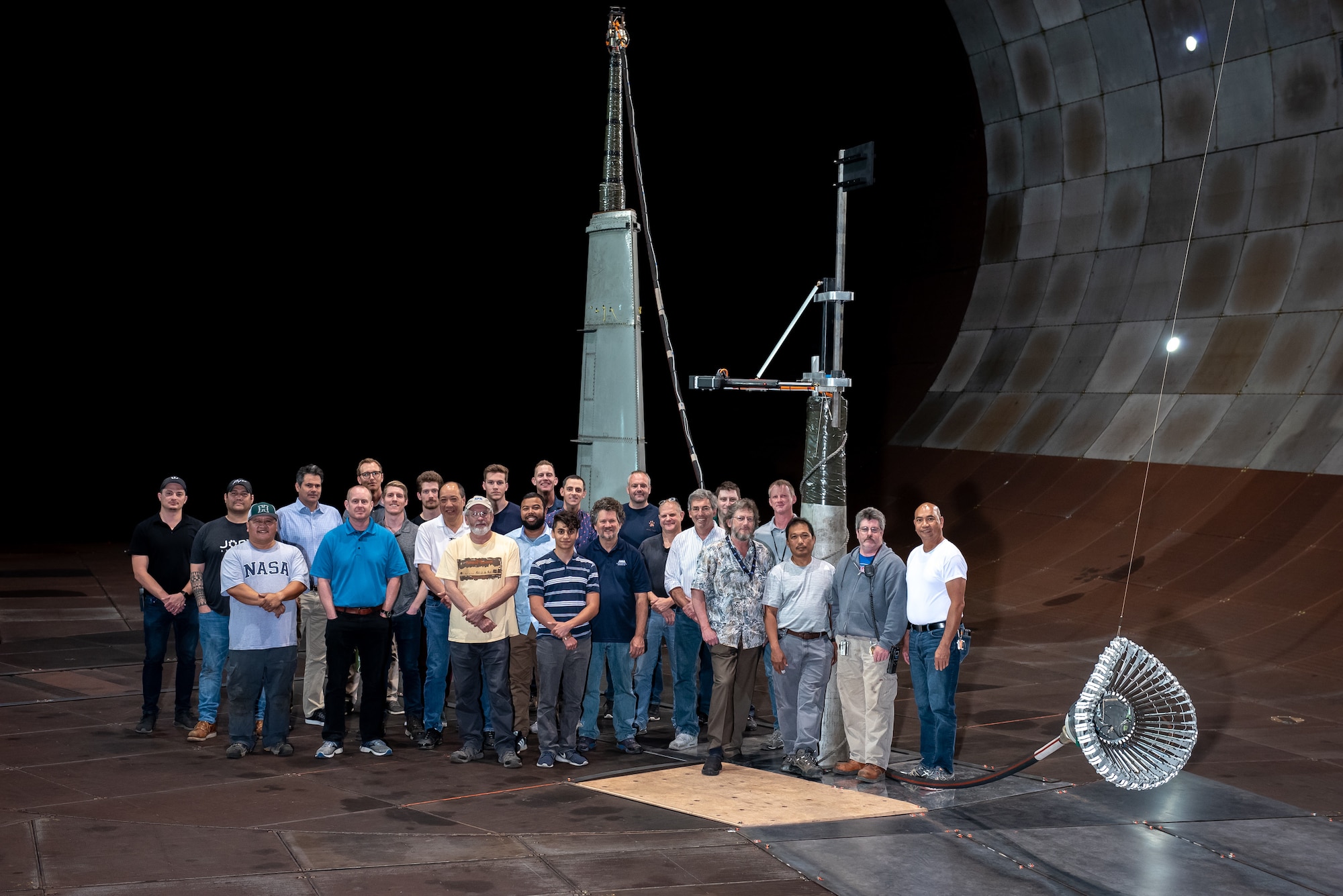 The team responsible for the testing of the integrated Actively Stabilized Refueling Drogue System and Optical Reference System stands with the tested hose and drogue system in the 40- by 80-foot wind tunnel at the Arnold Engineering Development Complex National Full-Scale Aerodynamics Complex, located in the NASA Ames Research Center at Moffett Field in Mountain View, California. The NFAC test team consisted of both Department of Defense and Test Operations and Sustainment contract employees from National Aerospace Solutions. The team included researchers, engineers, technicians and mechanics. (Courtesy photo)