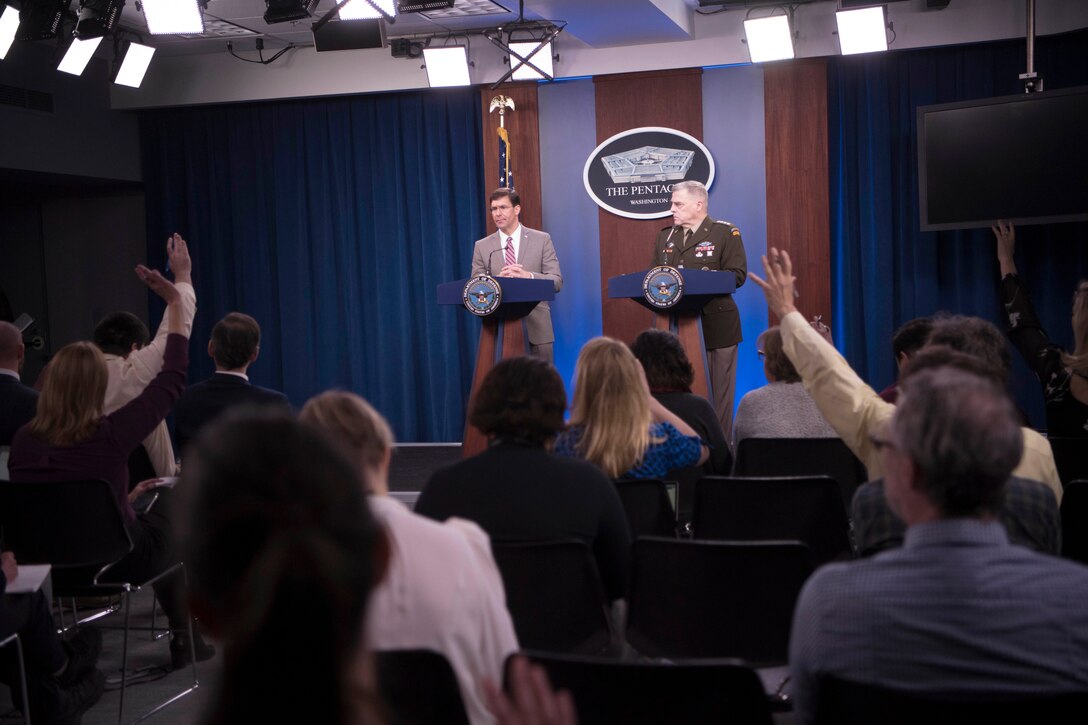 Reporters raise their hands as Defense Secretary Dr. Mark T. Esper and Army Gen. Mark A. Milley stand at lecterns.