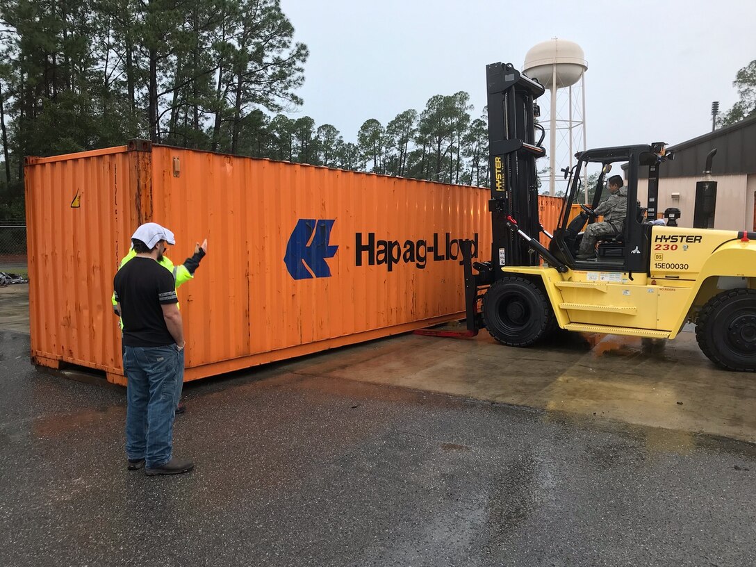 Active duty and civilian personnel from  Hurlburt Field help move a container containing wreckage from a CV-22 Osprey mishap in 2012 as it awaits hazardous waste disposal.