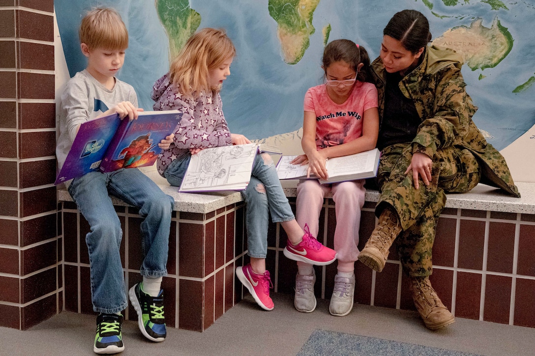 A sailor and three kids sit in front of a map and read books.