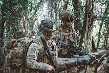 two men in green camouflage uniforms with camouflage paint hold military rifles in the jungle.