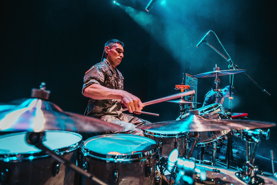 A soldier on a dark stage plays drums.