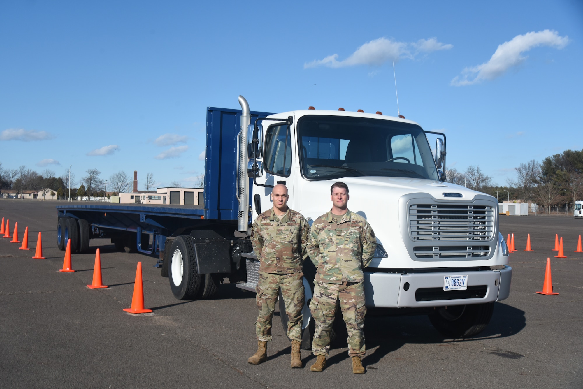 Two Airmen pose in front of a vehicle.