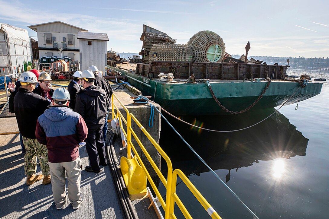 Leaders watch a barge get loaded with scrap.