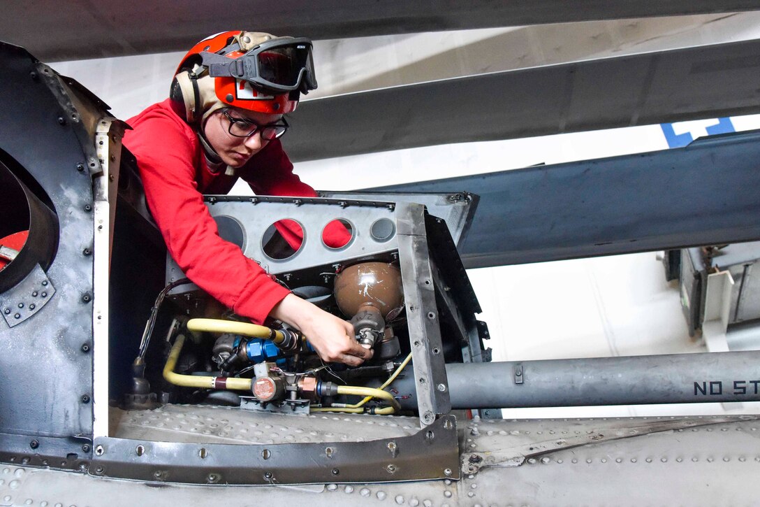 A sailor tightens fire bottle cad on an aircraft.