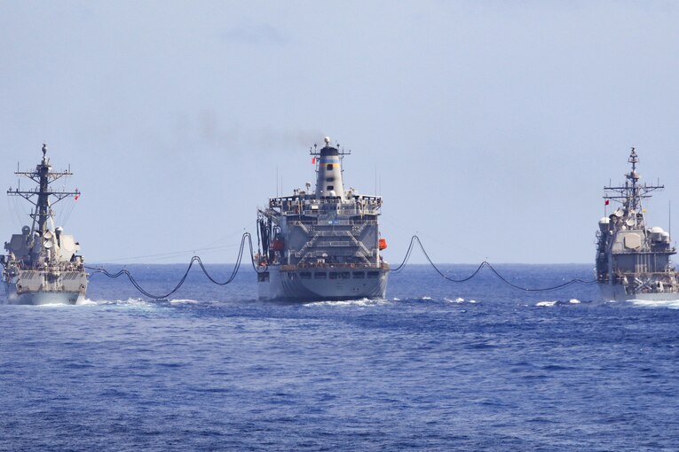 Three military ships steam next to each other in the ocean.