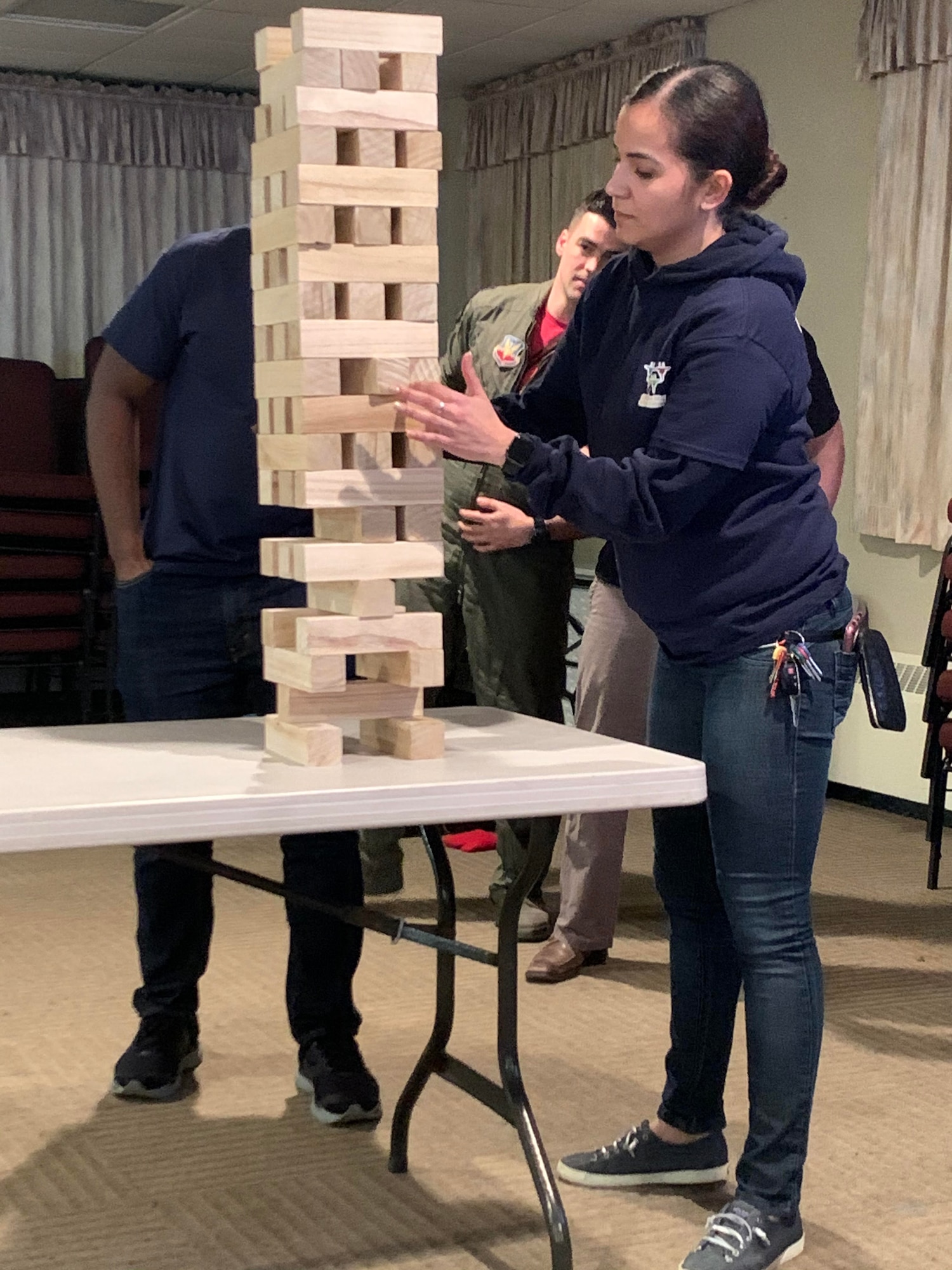 Airman 1st Class Mabell Teixeira of the 104th Force Support Squadron removes a game piece from the Jenga tower with intense concentration during the last competition against the officers. At the same time, the officers strategize their next move during the 104th Fighter Wing’s 2nd annual Officer vs. Enlisted Olympic games, Feb. 1, 2020. The enlisted and the officers took part in a friendly competition as part of the Wing’s camaraderie with the final score of enlisted 14 officers 13. (U.S. Air National Guard photo by Senior Master Sgt. Julie Avey)