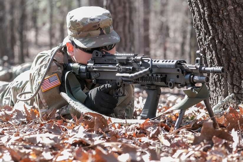 A soldier crouches on the ground with a machine gun.