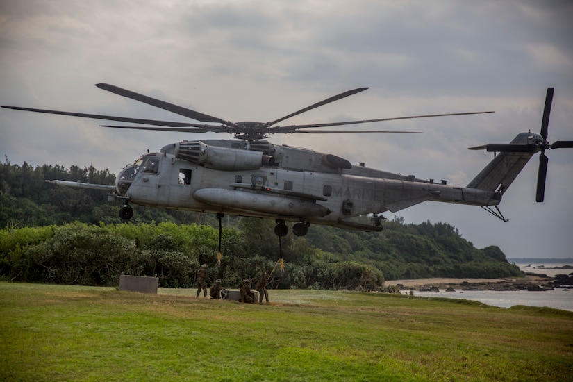 Helicopter hovers above four men in military uniforms.