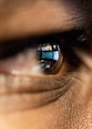 An extreme close up photograph of an Airman's eye shows the reflection of computer screens.