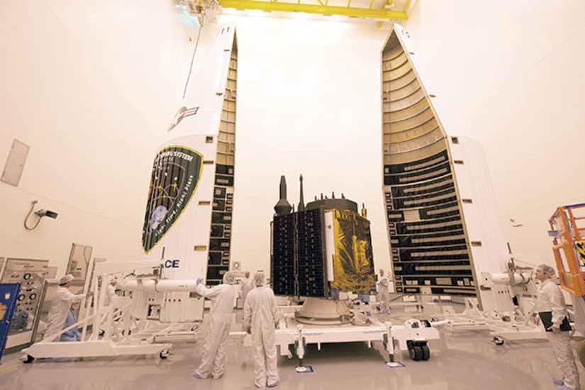 People wearing white “clean suits” load a satellite.