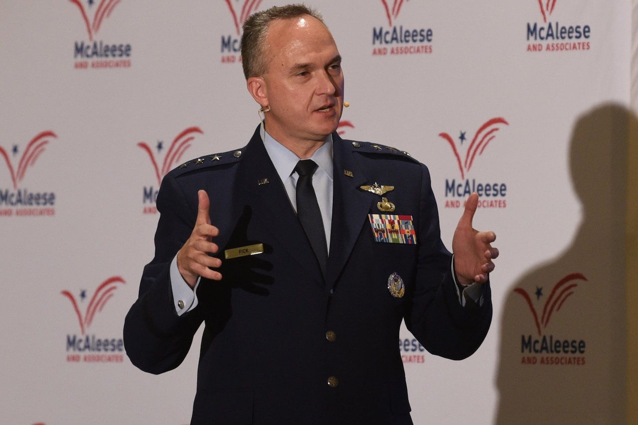 A man in a military uniform speaks into a microphone on a headset.