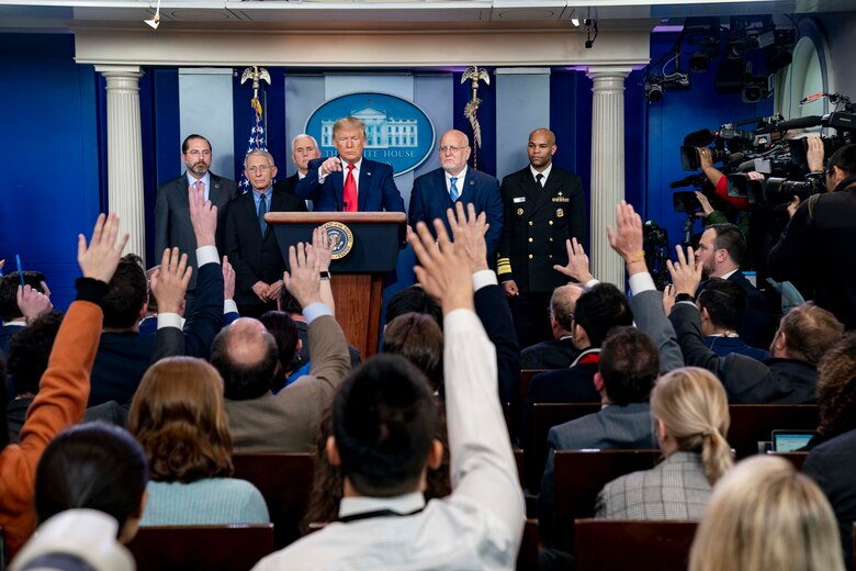 Men and women raise their hands as a man standing at a lectern points to one.