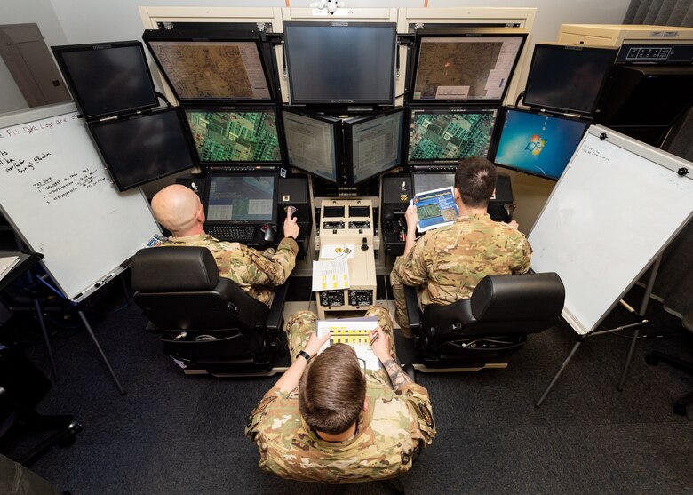 A pilot, sensor operator and an additional airman sit at an MQ-9 Reaper flight simulator.