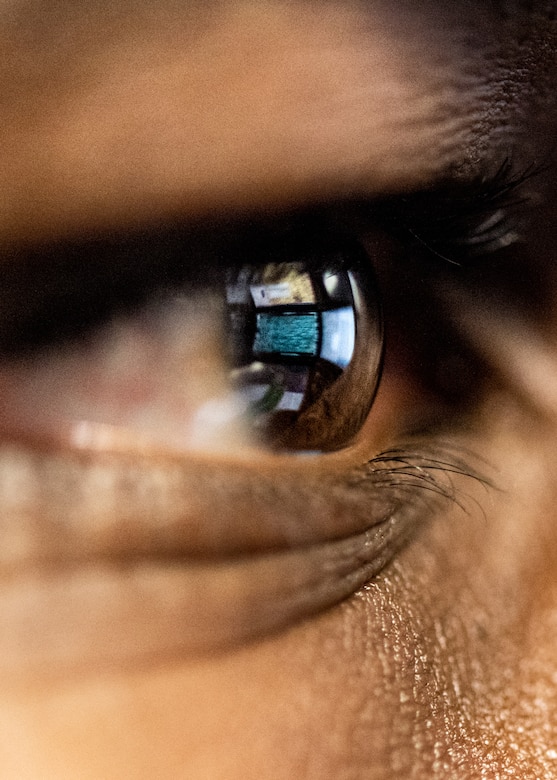An extreme close up photograph of an Airman's eye shows the reflection of computer screens.