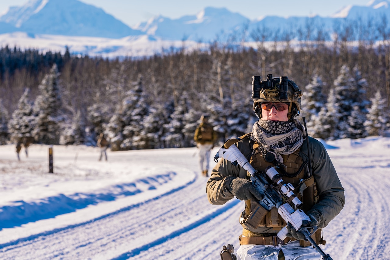 A marine carrying a gun walks in the snow.