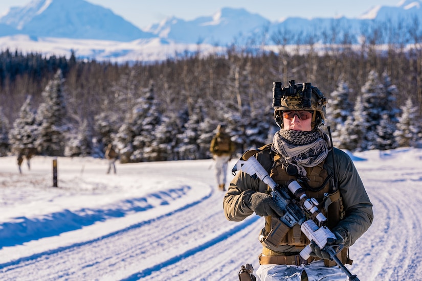 A marine carrying a gun walks in the snow.