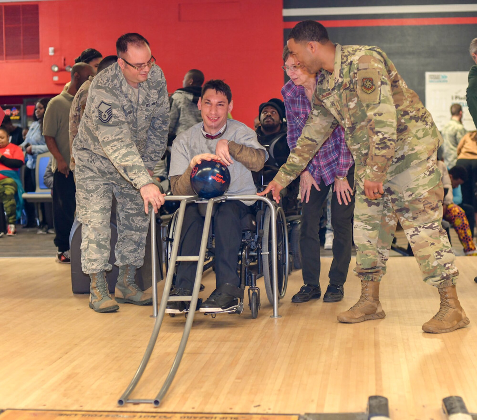 Master Sgt. Bryan Hess, 89th Maintenance Group, and Master Sgt. Jean Jean-Felix, 89th Communications Squadron, help Joshua Chartienitz, a participant in the tournament, bowl during the Special Olympics DC Adult Bowling Tournament in Hyattsville, Md., March 4, 2020. Over 30 Airman from Joint base Andrews volunteered at the event. (U.S. Air Force photo/Senior Airman Jalene A. Brooks)