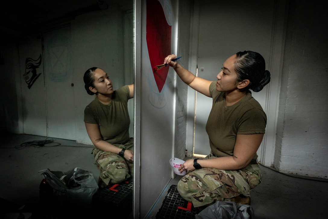 A service member paints a logo on a wall.