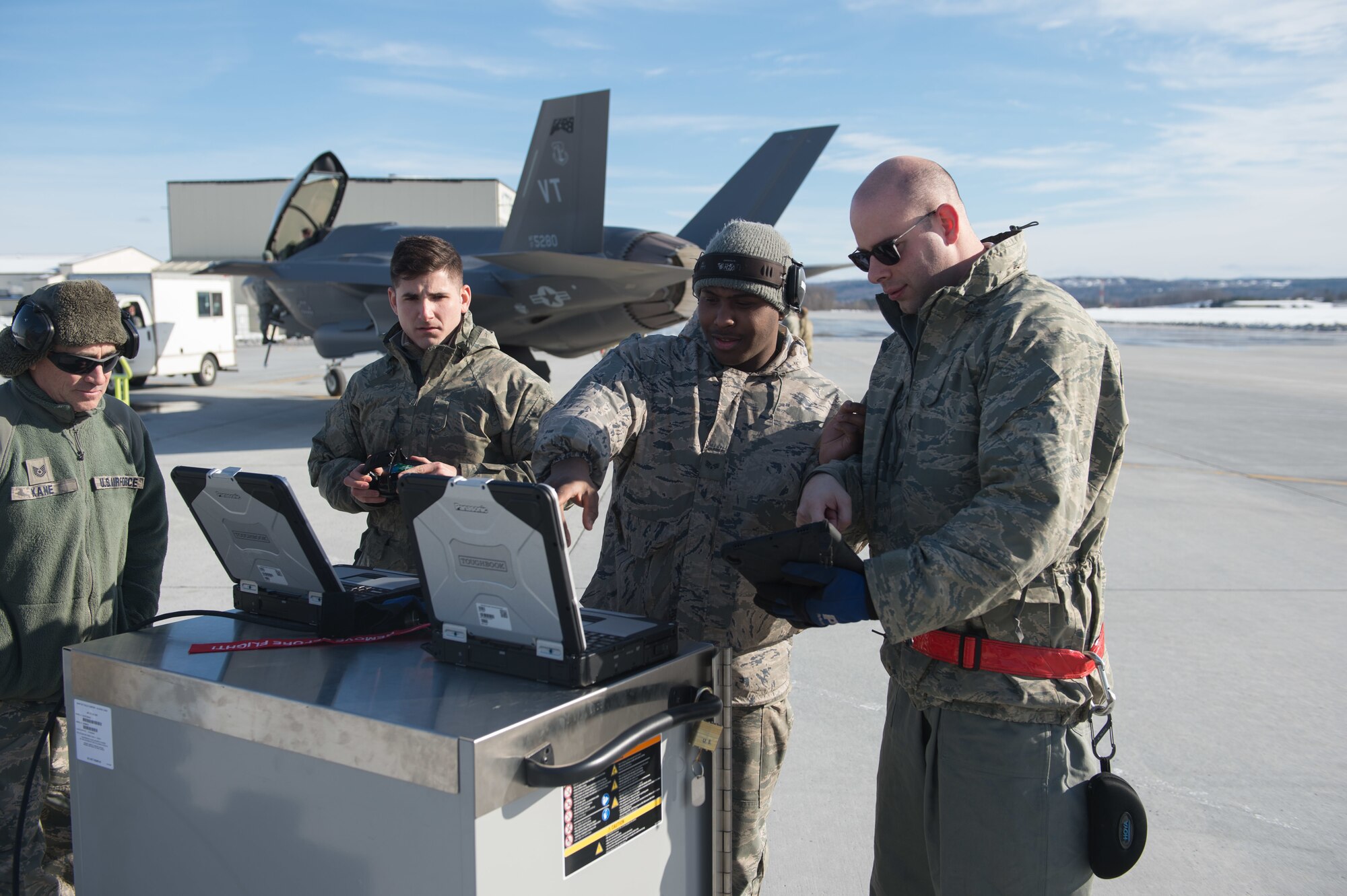 Crew chiefs assigned to the 158th Maintenance Group, 158th Fighter Wing, Vermont Air National Guard, work on a mobile device and computers on the flight line