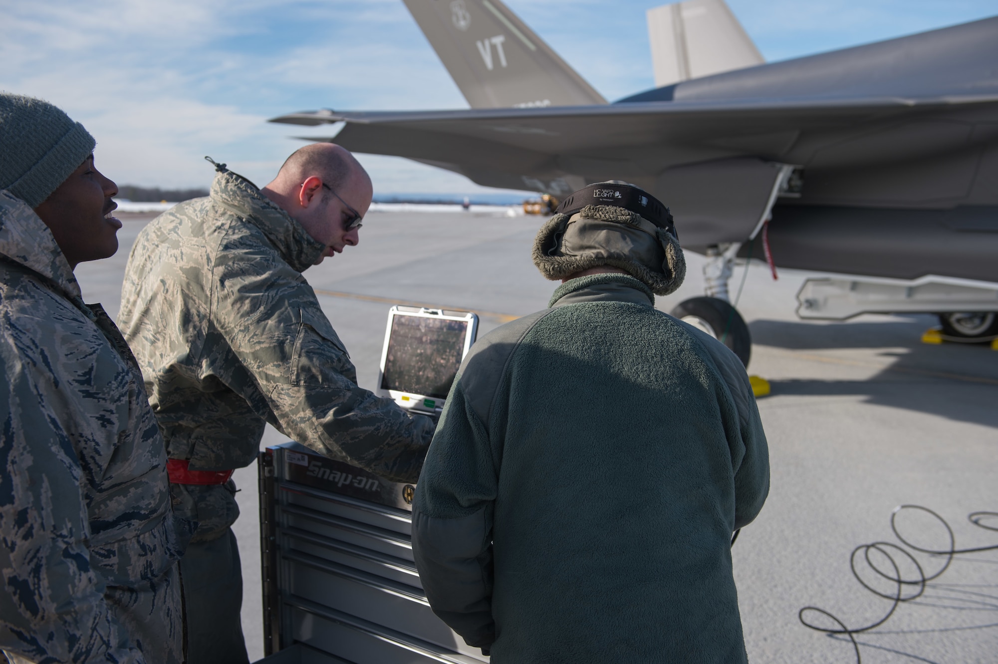 Crew chiefs assigned to the 158th Maintenance Group, 158th Fighter Wing, Vermont Air National Guard, work on a computer beside an F-35A Lightning II
