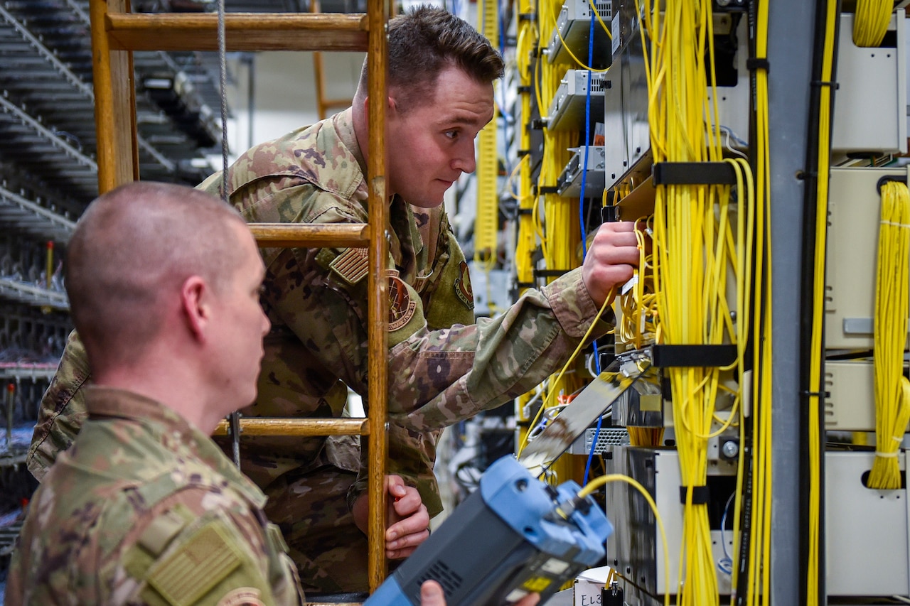 One service member and two men troubleshoot wiring.