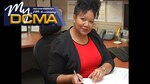 A woman, who is wearing a black blazer, reviews work materials, while sitting at her desk.