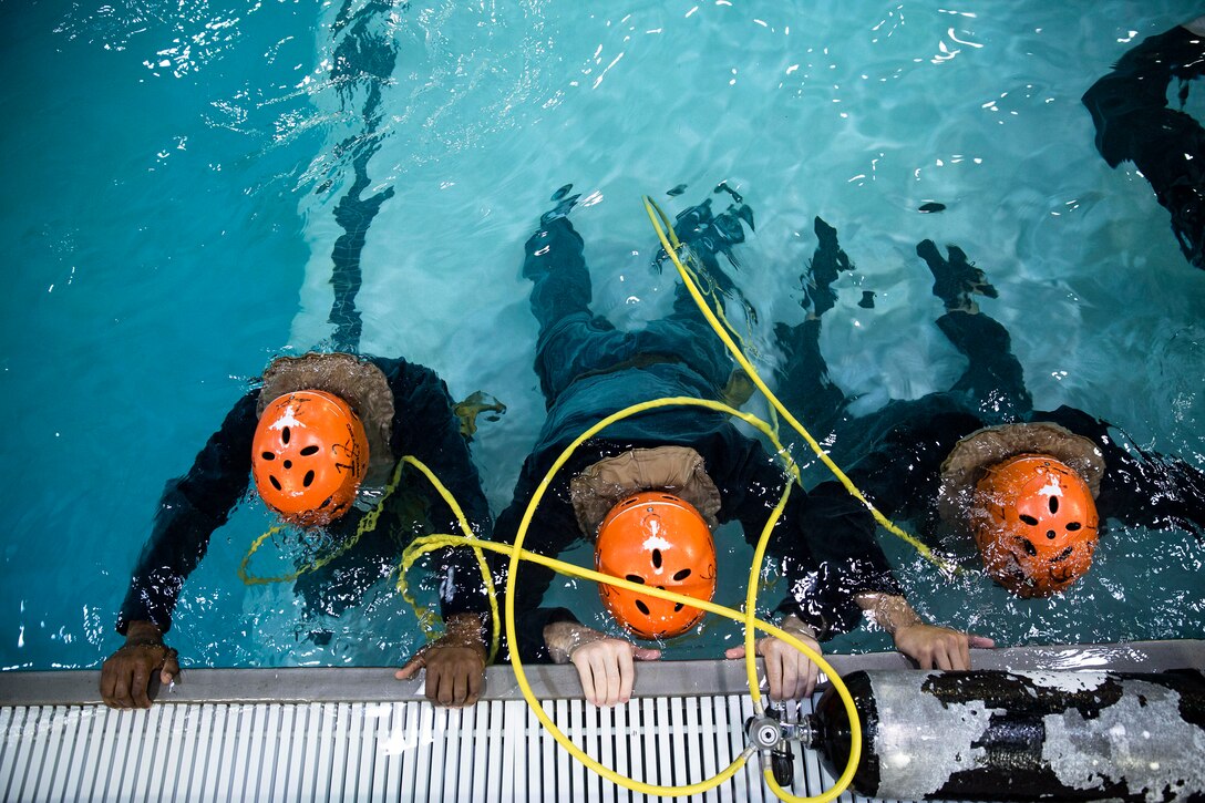 Three Marines hold on to the side of the pool while they are underwater.