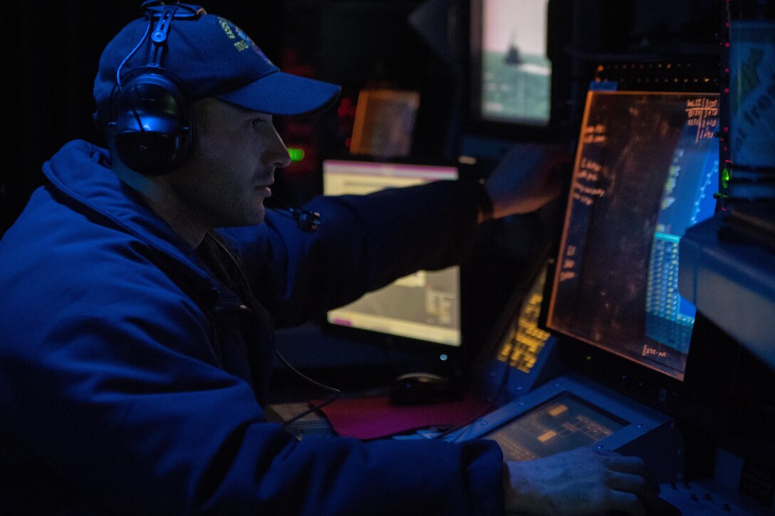 A man looks at a computer screen in a room with low lighting.