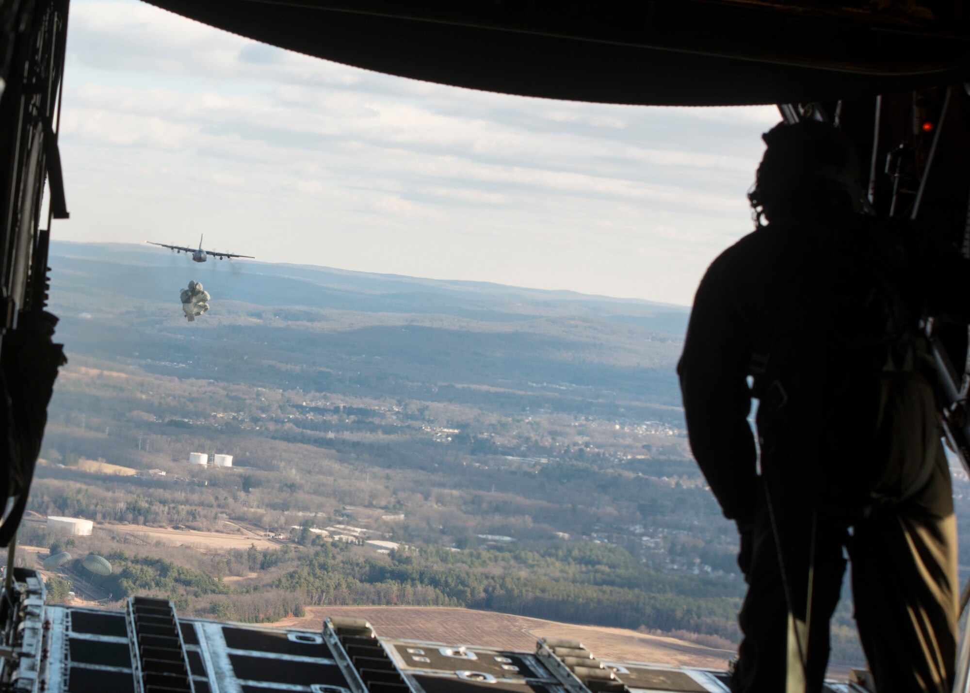 Master Sgt. Khaleef Graham, 118th Airlift Squadron loadmaster, watches a C-130H Hercules assigned to the 103rd Airlift Wing drop a heavy pallet over the drop zone at Westover Air Reserve Base, Chicopee, Mass. Jan. 15, 2020. Aircrews from the 103rd flew a two-ship formation and conducted airdrops with heavy pallets and container delivery systems, training key tactical airlift capabilities. (U.S. Air National Guard photo by Staff Sgt. Steven Tucker)