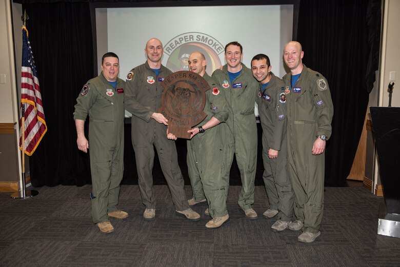 Airmen from the 20th Attack Squadron hold a trophy for winning a crud competition, a game historically held among the pilot community.