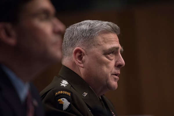 A man in a military uniform sits next to a man in a business suit.