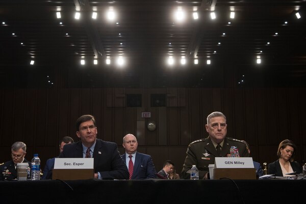 Two men sit behind a desk and testify.