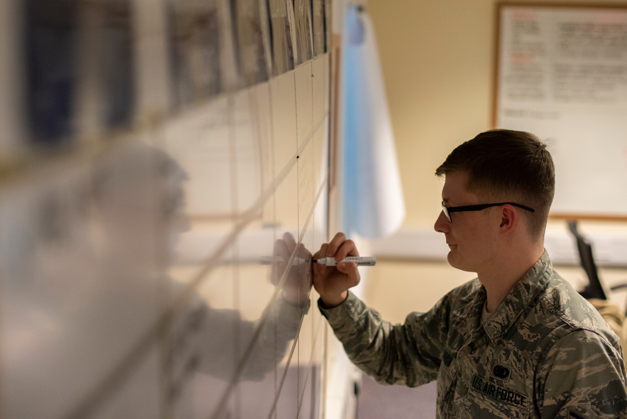 Airman 1st Class Ethan Morrow, 100th Logistics Readiness Squadron logistics apprentice, writes a deployment schedule on a whiteboard March 3, 2020, at RAF Mildenhall, England.  The installation deployment readiness cell manages the behind-the-scenes scheduling and planning for deployments in order to ensure Airmen are prepared to succeed on their mission. (U.S. Air Force photo by Airman 1st Class Joseph Barron)