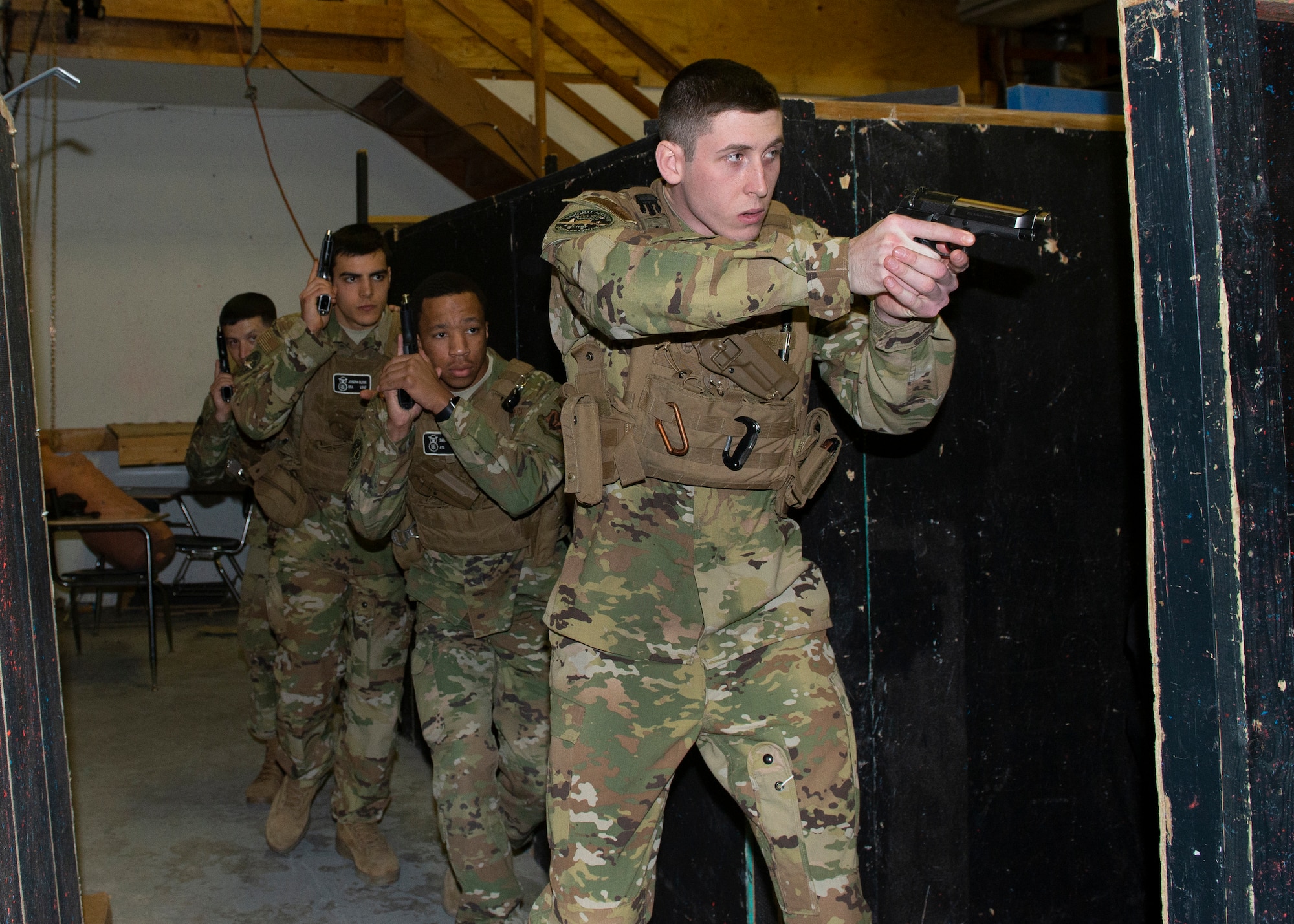 photograph of four Airmen with weapons in their hands as they move along a wall inside training area