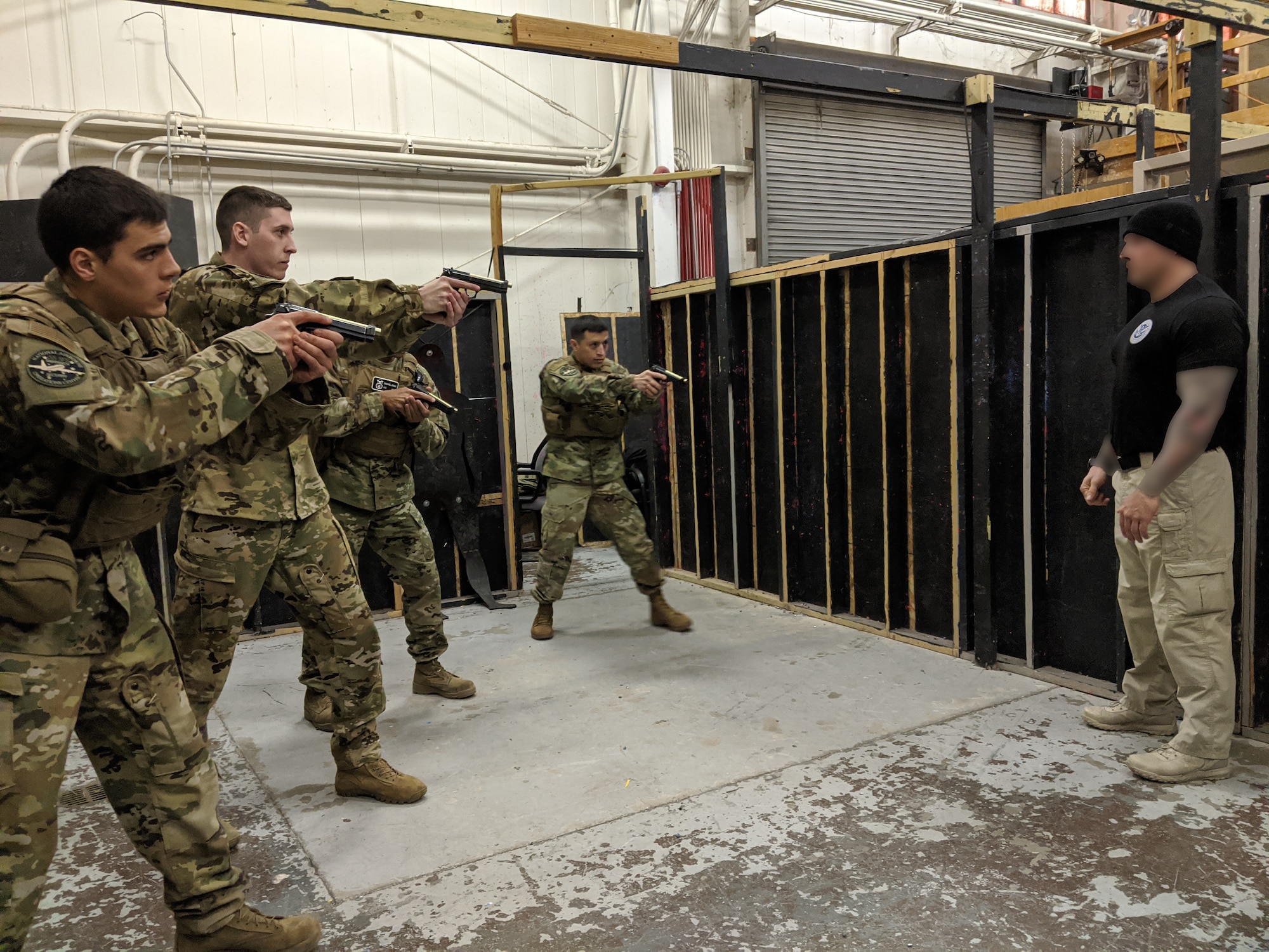 photograph of four airmen holding weapons as they train with federal air marshal as he observes their techniques.