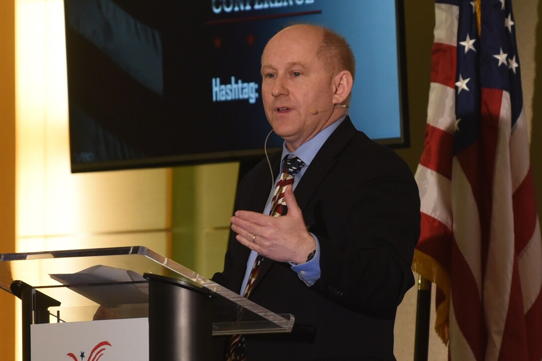 Man speaks from behind a lectern; the U.S. flag is behind him.