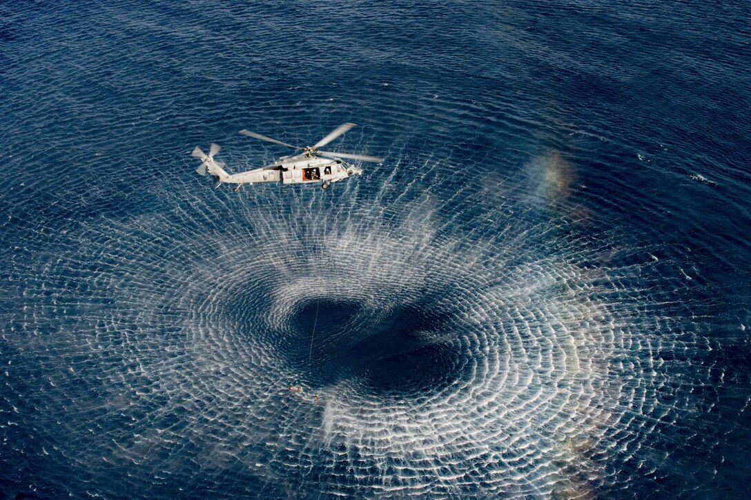 A Navy helicopter flies over a body of water.