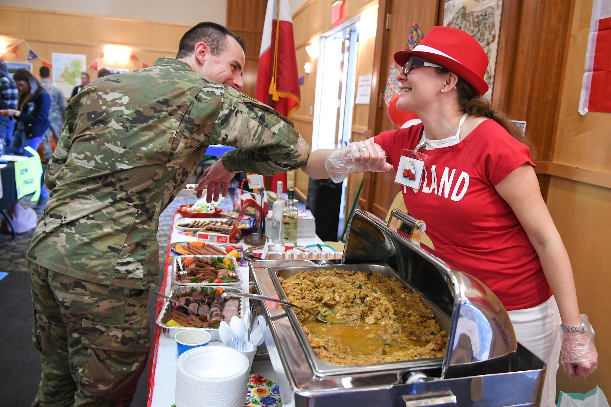 First Lt. Jamee Boyer, Air Force Life Cycle Management, elbow bumps AÍicia Pogovzelska, from Poland, after tasting her dish at the International Culinary Tasting Buffet March 4, 2020, at Hill Air Force Base, Utah. The event was hosted by the Hill AFB foreign liaison officers and featured food, drinks, and cultural education from 15 different countries. (U.S. Air Force photo by Cynthia Griggs)