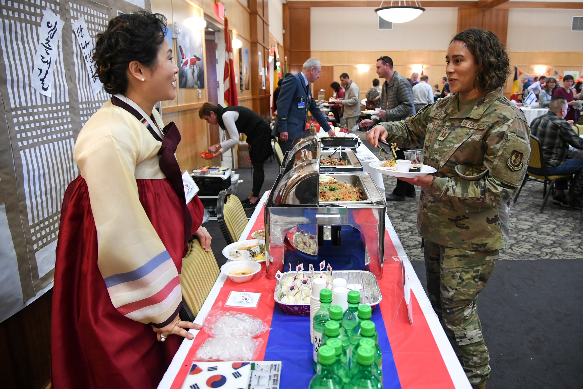 Capt. Indigo Blakely, Air Force Life Cycle Management Center, talks about Korean food with Kyungmin Lee at the International Culinary Tasting Buffet March 4, 2020, at Hill Air Force Base, Utah. The event was hosted by the Hill AFB foreign liaison officers and featured food, drinks, and cultural education from 15 different countries. (U.S. Air Force photo by Cynthia Griggs)