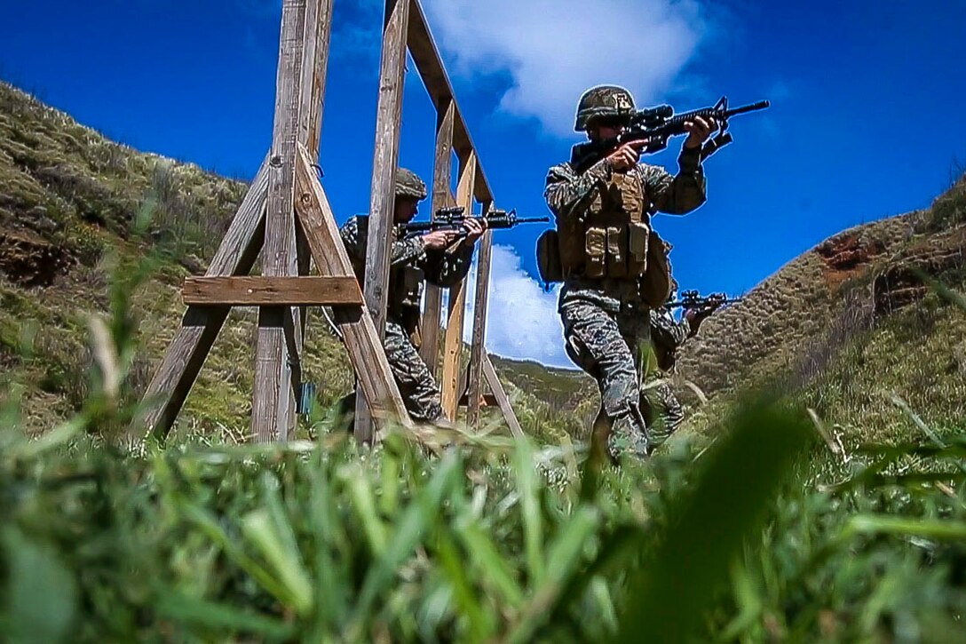 Three Marines walk through a doorway pointing their weapons.