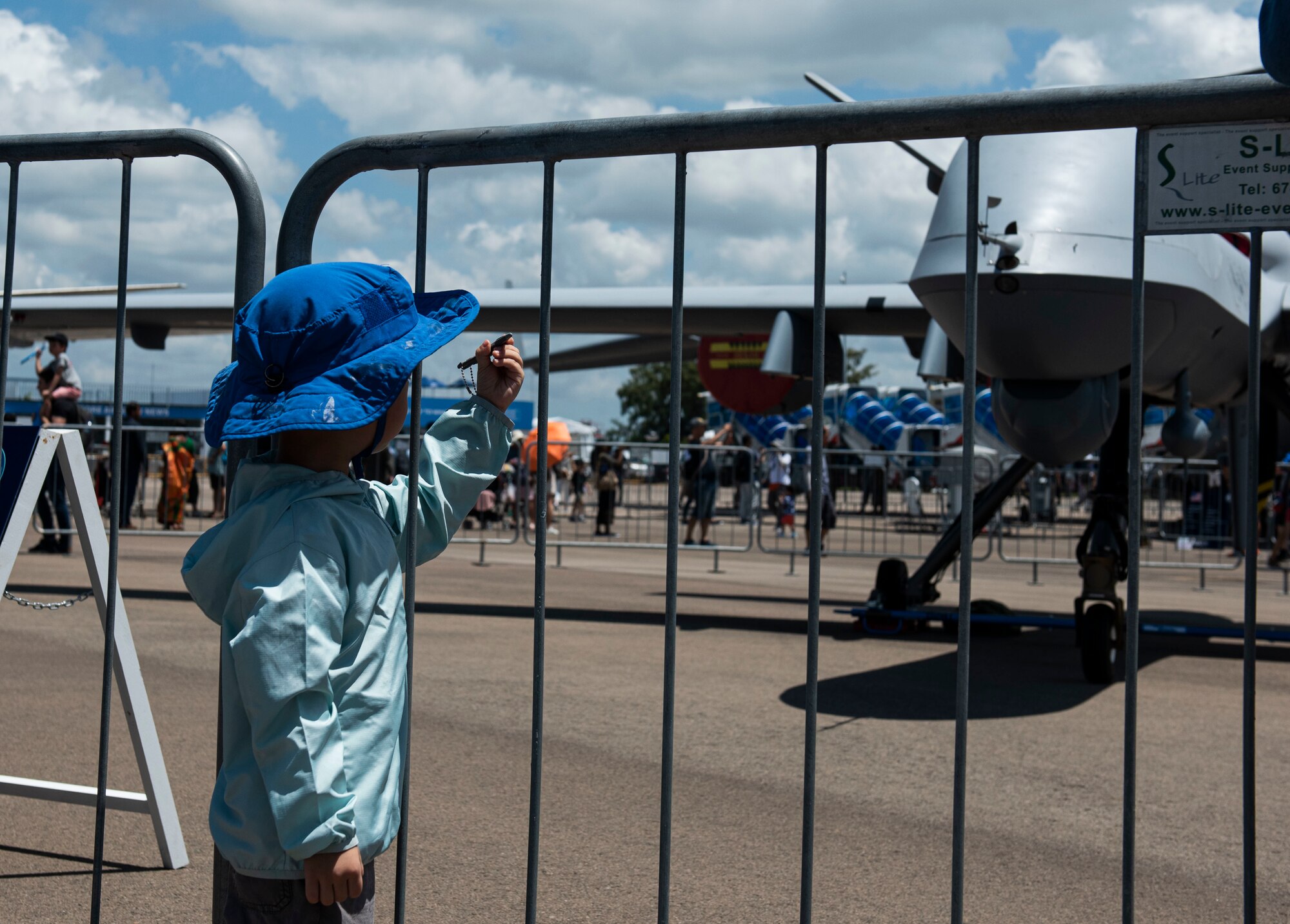 A child marvels at his toy plane while he stands in front of the MQ-9 Reaper at Singapore Airshow.