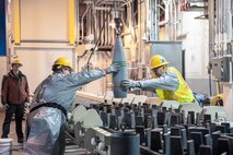 Blue Grass Chemical Agent-Destruction Pilot Plant workers place the first 8-inch projectile containing GB nerve agent in a tray to begin the destruction process in the Munitions Demilitarization Building in Richmond, Kentucky, Jan. 16, 2020.
