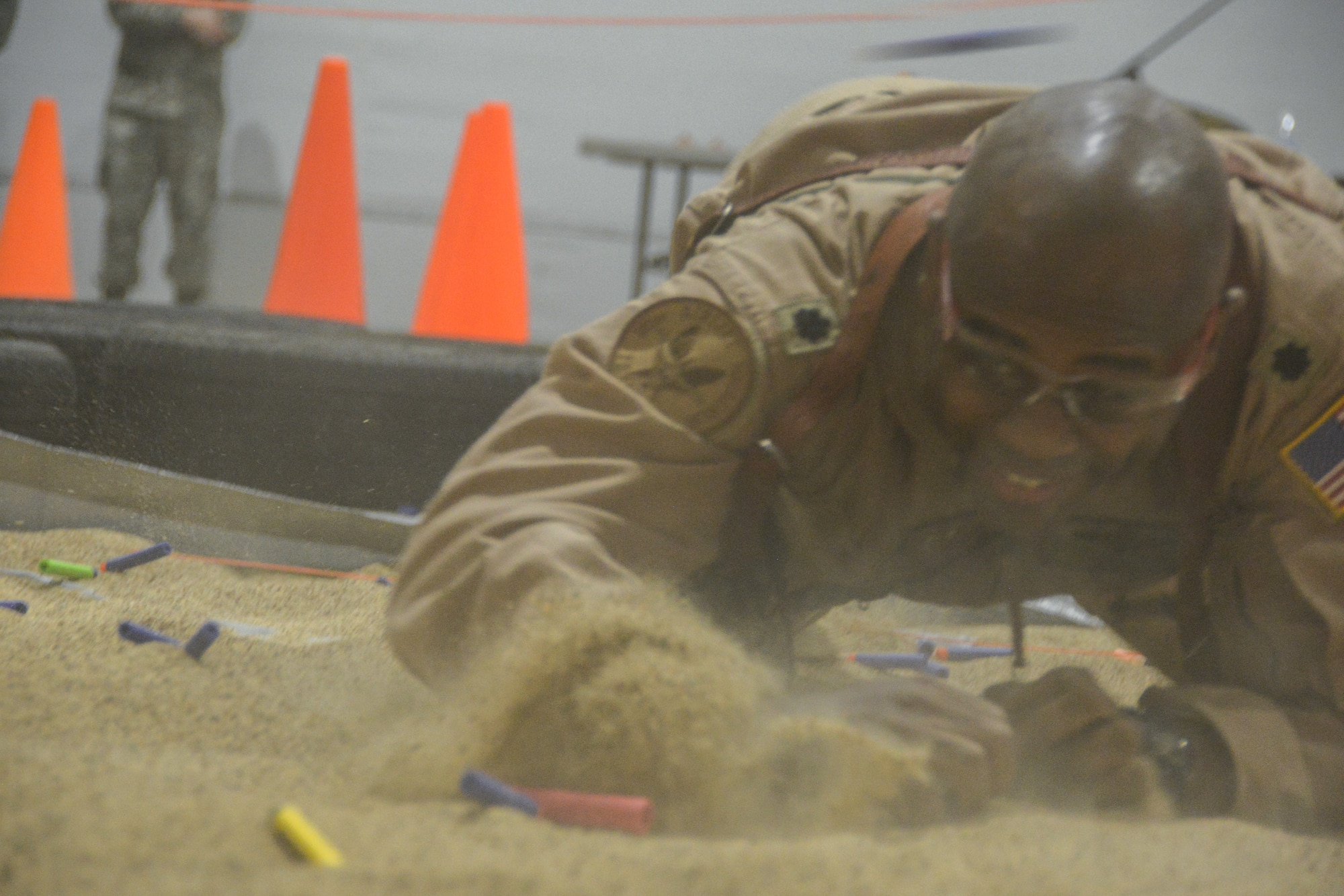 A Texas Air National Guard Lieutenant Colonel low-crawls through sand while being pelted with foam darts.