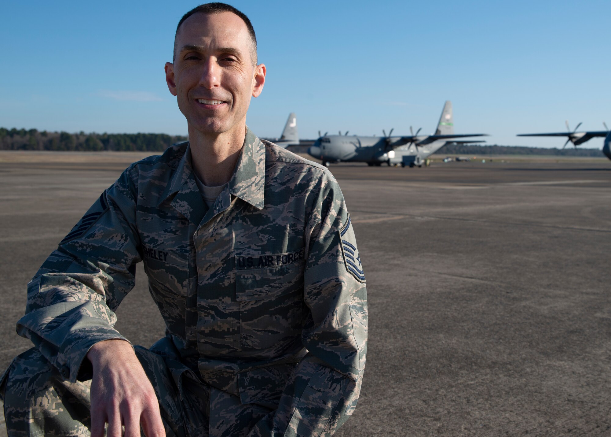 Master Sgt. Matthew Sheley poses on the flight line with C-130J aircraft in the background.