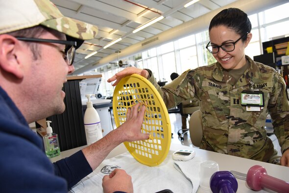 U.S. Army Capt. Jacqueline Tamayo, right, Landstuhl Regional Medical Center occupational therapy assistant chief, coaches Petty Officer 2nd Class Even Parker, Armed Forces Network Europe photographer, through hand strength exercises at LRMC, Germany, March 3, 2020. A patient would go to the occupational therapists at LRMC for issues including PTSD resulting from combat or sexual trauma, traumatic brain injury, wrist fracture, tendon laceration, a broken finger, and memory or movement problems resulting from a stroke.