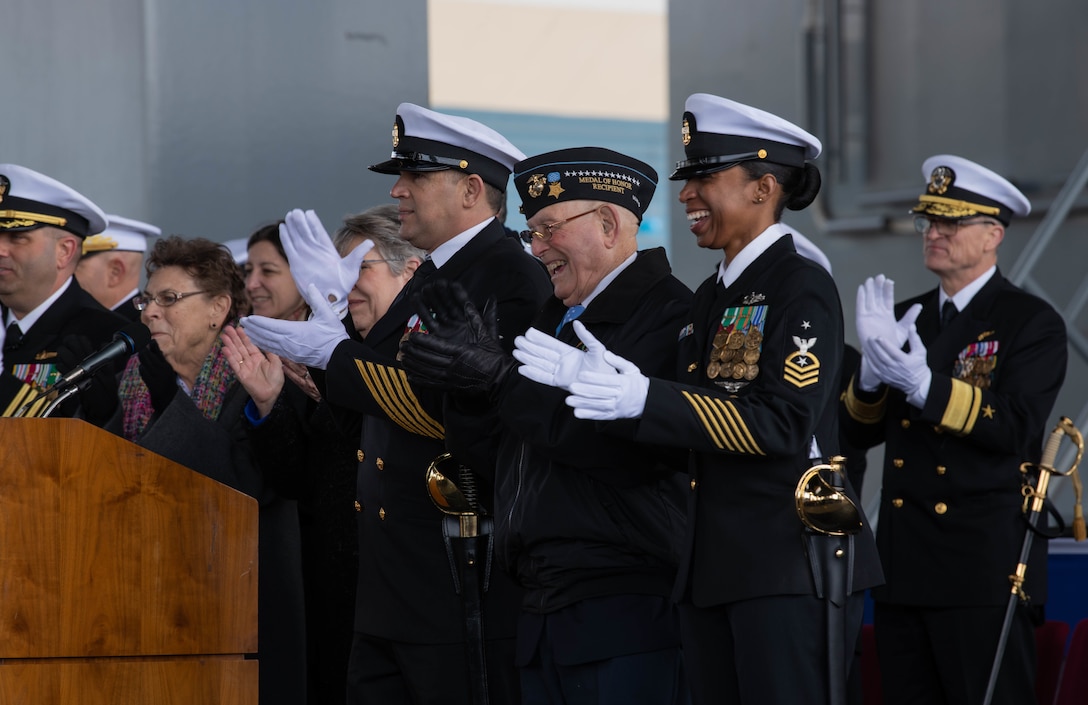 Members of the ship commissioning committee clap and enjoy the “man our ship and bring her to life” part of the ceremony, March 7.