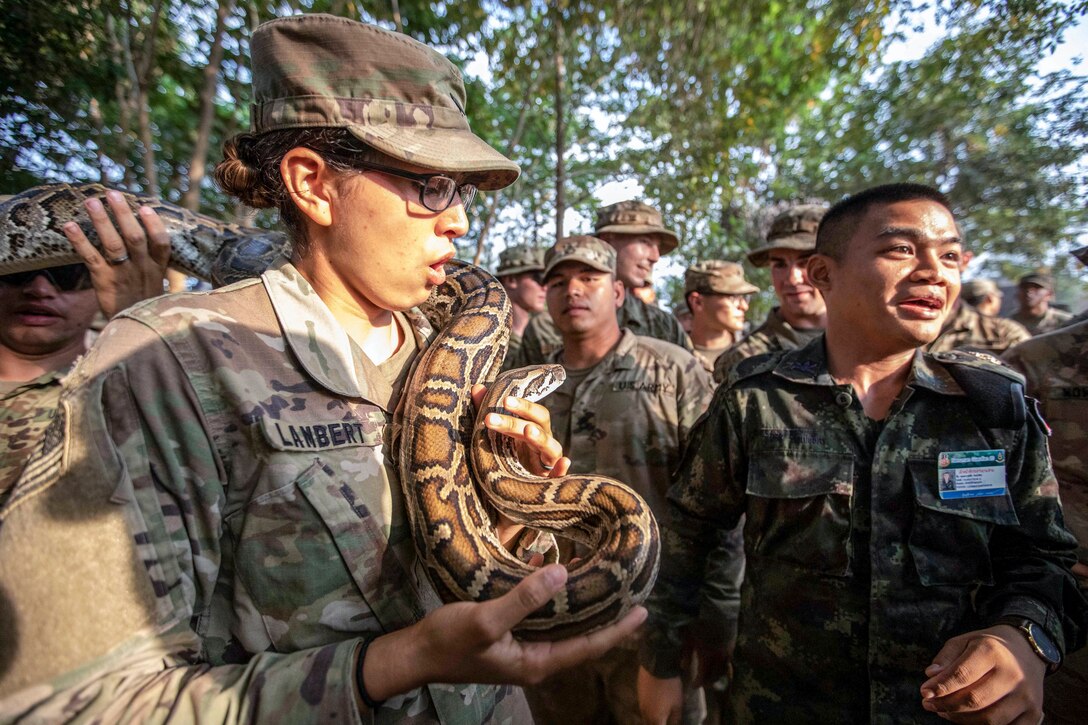 A soldier holds a snake on her shoulder as U.S. and Thai soldiers watch in the jungle.