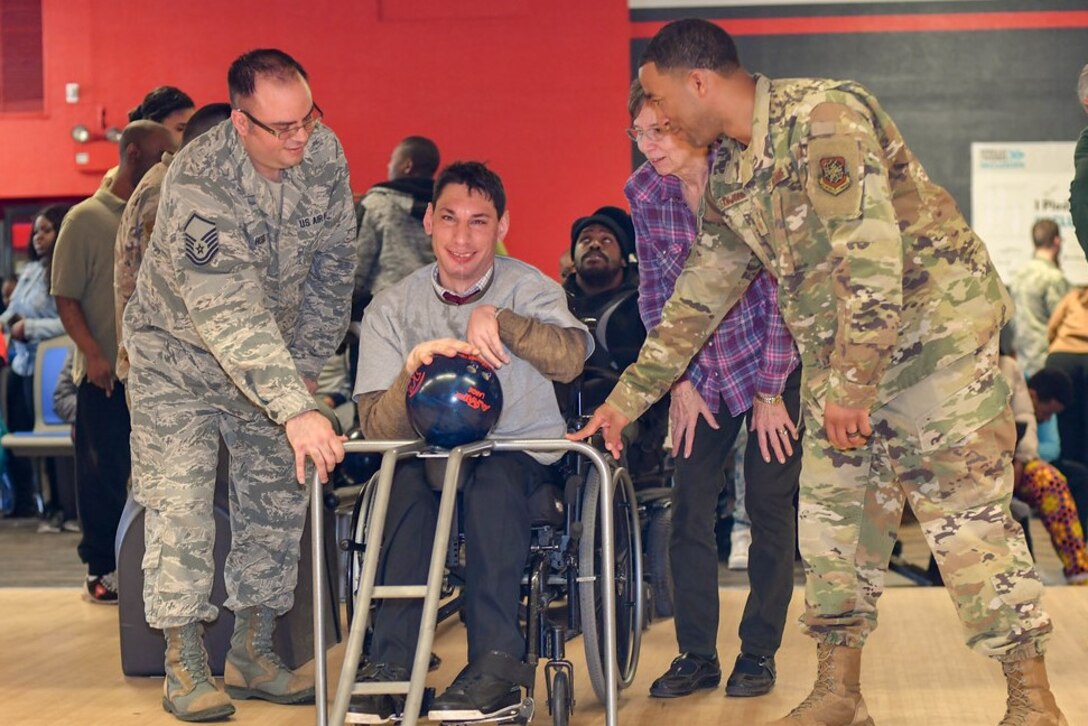 Master Sgt. Bryan Hess, 89th Maintenance Group, and Master Sgt. Jean Jean-Felix, 89th Communications Squadron, help Joshua Chartienitz, a participant in the tournament, bowl during the Special Olympics DC Adult Bowling Tournament in Hyattsville, Md., March 4, 2020. Over 30 Airman from Joint base Andrews volunteered at the event. (U.S. Air Force photo/Senior Airman Jalene A. Brooks)